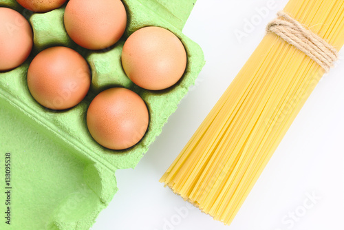 Eggs in paperboard egg carton and spaghetti on white background