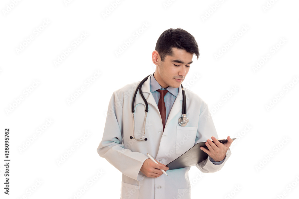young serious brunette man doctor in uniform with stethoscope on his shoulders make notes isolated on white background young serious brunette man doctor in uniform with stethoscope on his shoulders make notes isolated on white background