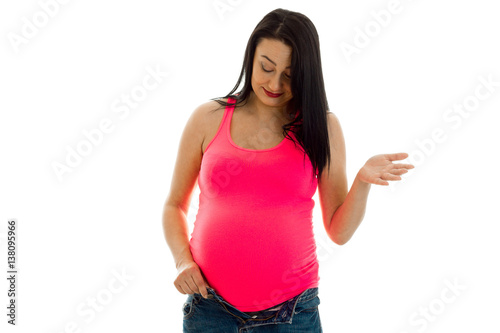 pretty brunette pregnant woman in bright pink shirt looking at her belly isolated on white background