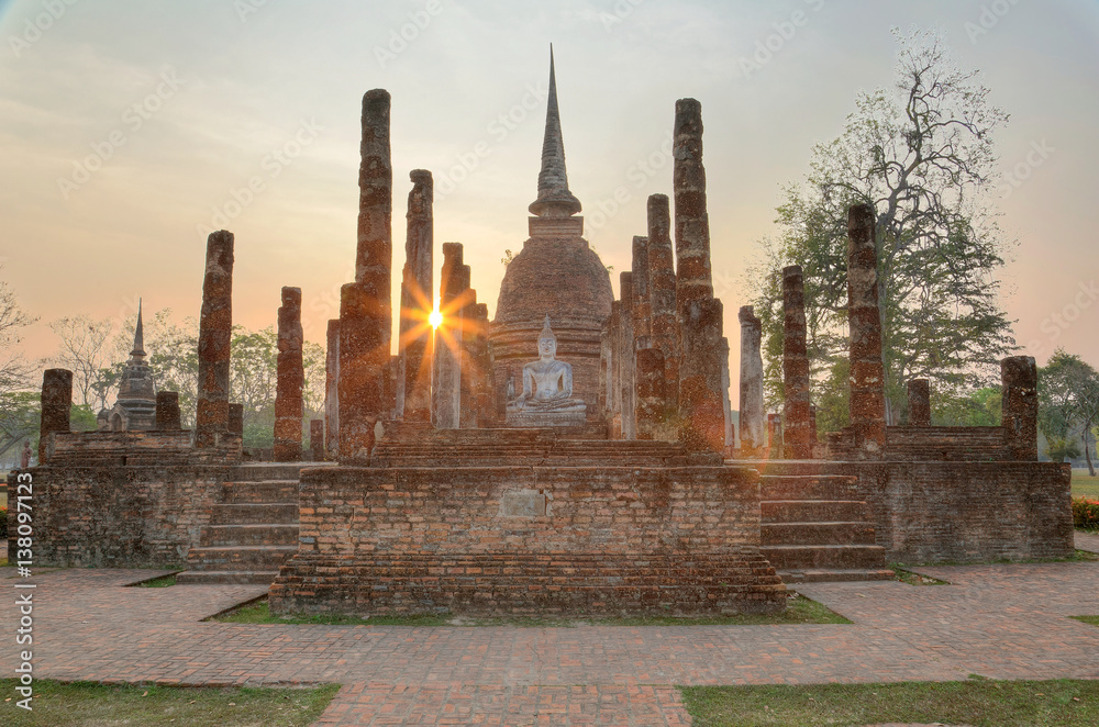 Naklejka premium Sunset scenery of Wat Sa Si in Sukhothai Historical Park with setting sun in background and a statue of seated Buddha in the shrine of a ruined temple ~ A beautiful UNESCO heritage site in Thailand
