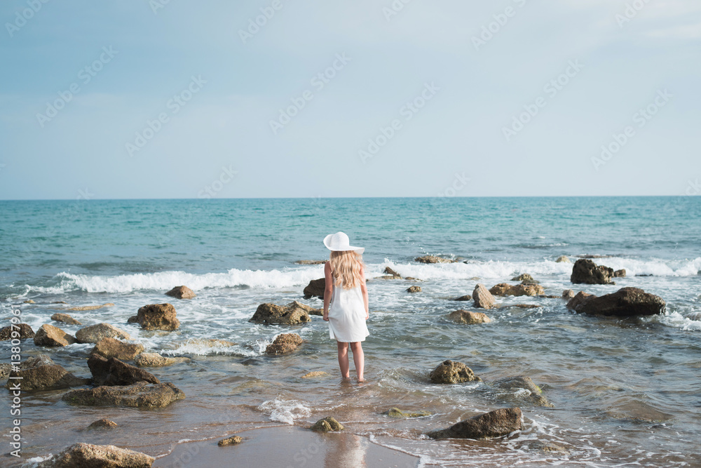 девочка в шляпе и белом платье гуляет по берегу моря