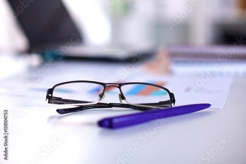 A note book, laptop, pen, graph paper document on the office desk table behind white blind