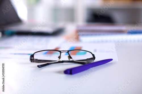 A note book, laptop, pen, graph paper document on the office desk table behind white blind
