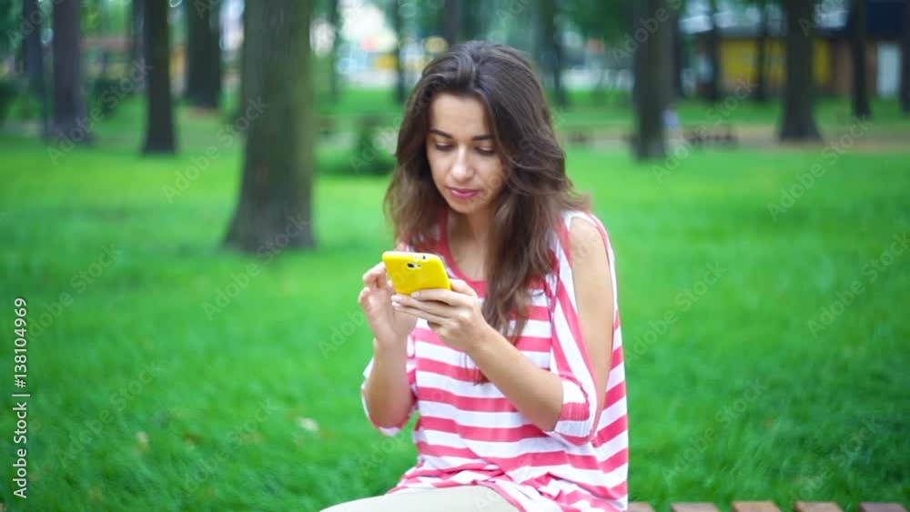 young woman sitting on a bench in the summer park with a smartphone.