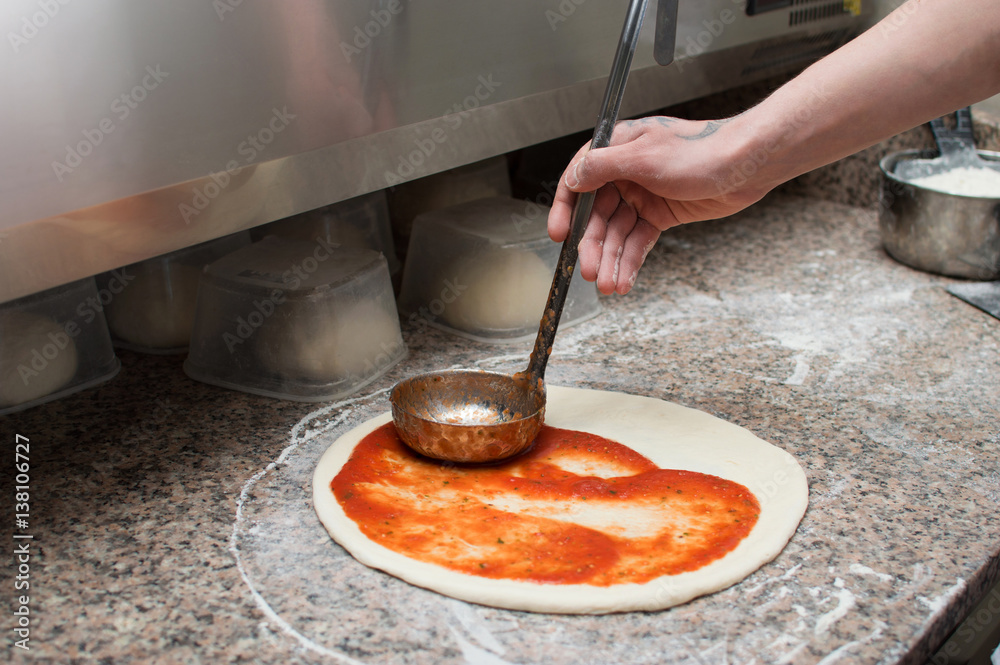 Male chef smears red sauce spicy pizza. Raw dough preform. Production and delivery of pizza