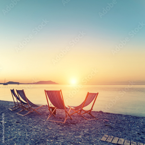 Beach loungers on the deserted coast sea at sunrise.