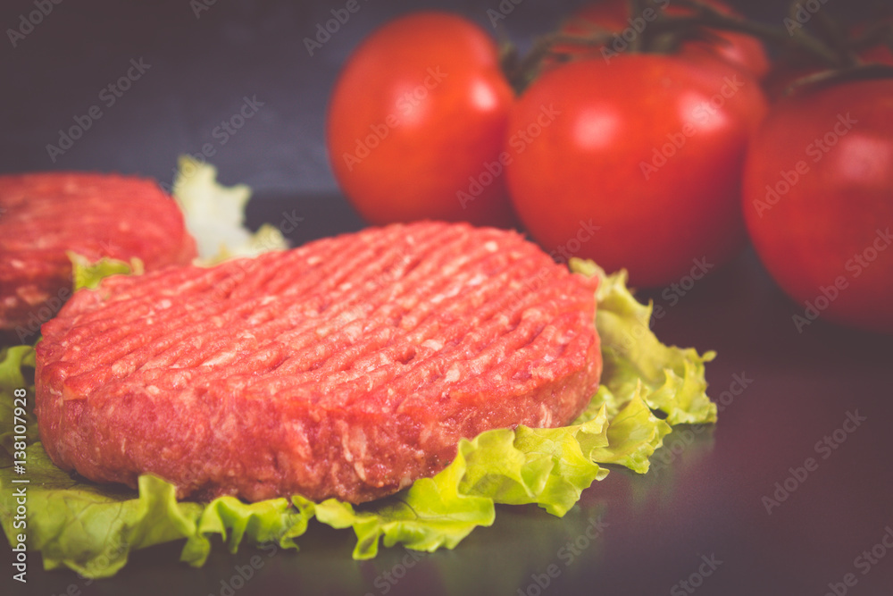 Raw burgers with lettuce on a gray background. Tomatoes, peppers chilli. Raw burgers with lettuce on a gray background. Tomatoes, peppers chilli.