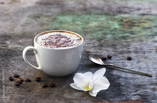 A cup of hot coffee and orchid flower on the wooden background. Traditional drink cappuccino or cocoa Wooden background Orchid flower