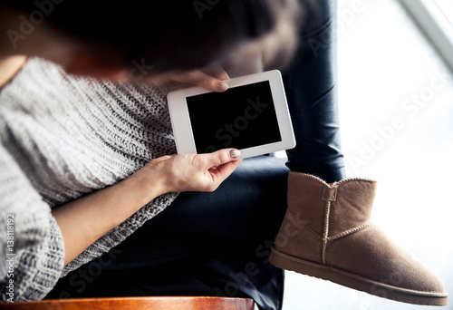 A girl holding a tablet in hands, reader with a nice manicure. Leather trousers, ugg boots. Fashion, style, learning, modern, recreation