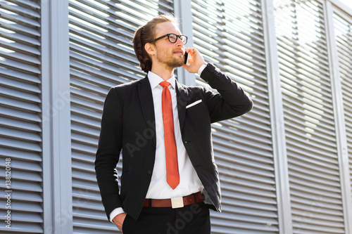 A businessman with a beard and glasses talking on the phone.