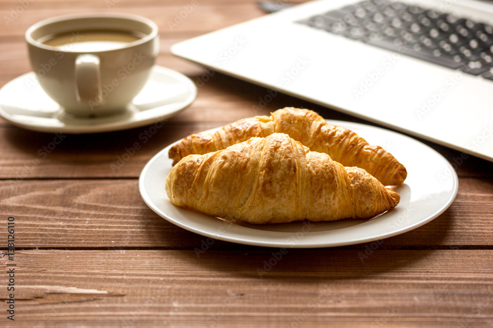 Business lunch with croissant and laptop on wooden desk