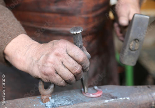 hand elder blacksmith who uses an iron awl over a large anvil