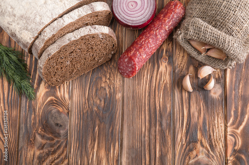 salami, bread, onion, garlic in a linen pouch and dill on an old wooden table.