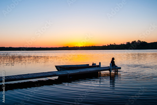 Woman on dock on tranquil lake at sunset in Minnesota