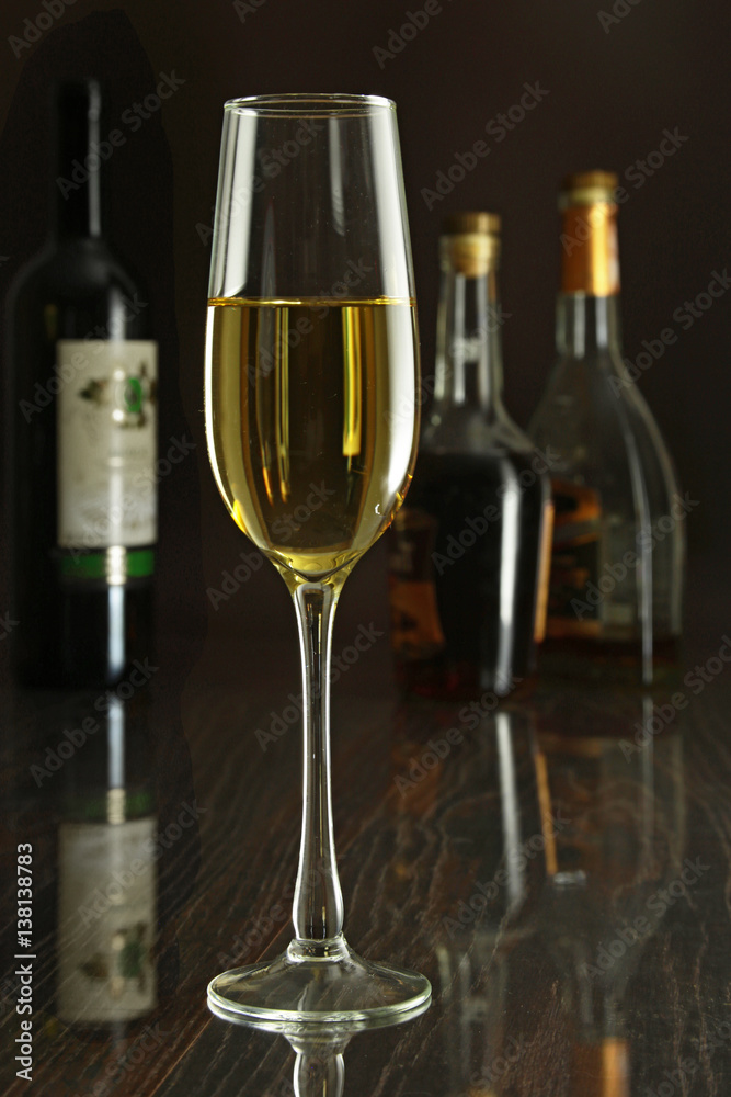 Glass of white wine on mirror table. bottles in a bar on the background