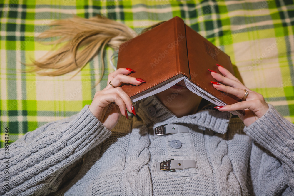 Obraz premium The girl lies and hides his face behind a book.