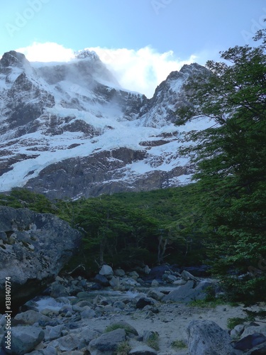Creek flows through valle frances in the shadow of large snow covered cliffs and peak of Torres del Paine National Park. 