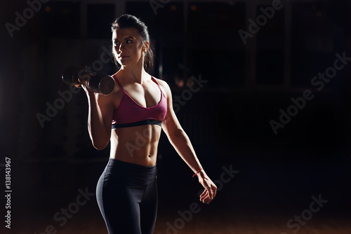 Silhouette of sporty young woman doing weight lifting against black background