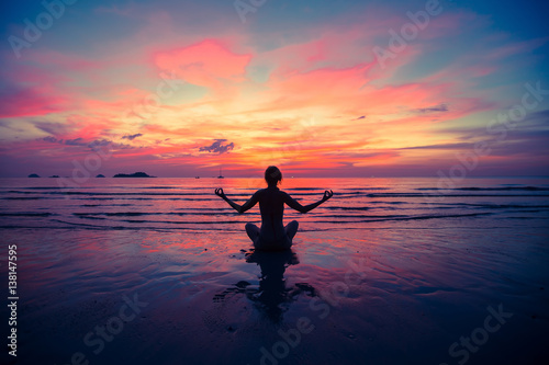 Silhouette young woman practicing yoga on the beach at sunset. © De Visu