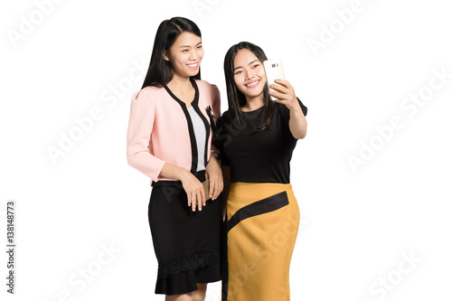 portrait of two beautiful asian business woman smiling and making a selfie with smart phone. Isolated on white background with copy space