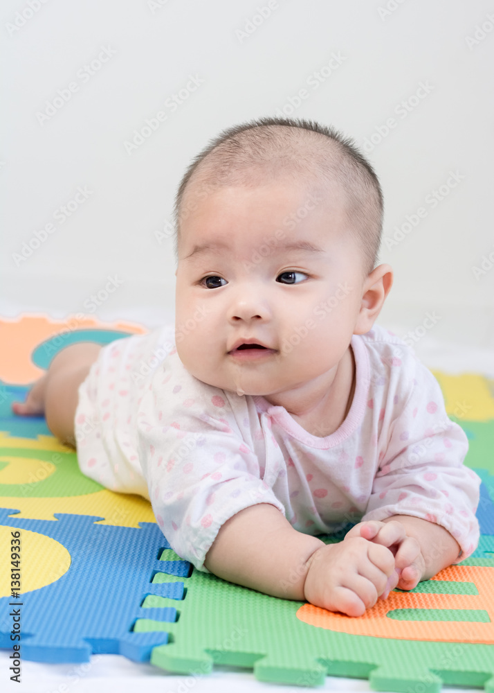 Portrait of a little adorable newborn infant baby girl with saliva lying on the tummy on colorful eva foam and looking in camera indoors Portrait of a little adorable newborn infant baby girl with saliva lying on the tummy on colorful eva foam and looking in camera indoors