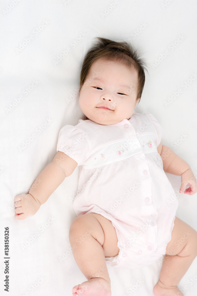 Portrait of a little adorable infant baby girl lying on back on blanket and looking in camera indoors Portrait of a little adorable infant baby girl lying on back on blanket and looking in camera indoors