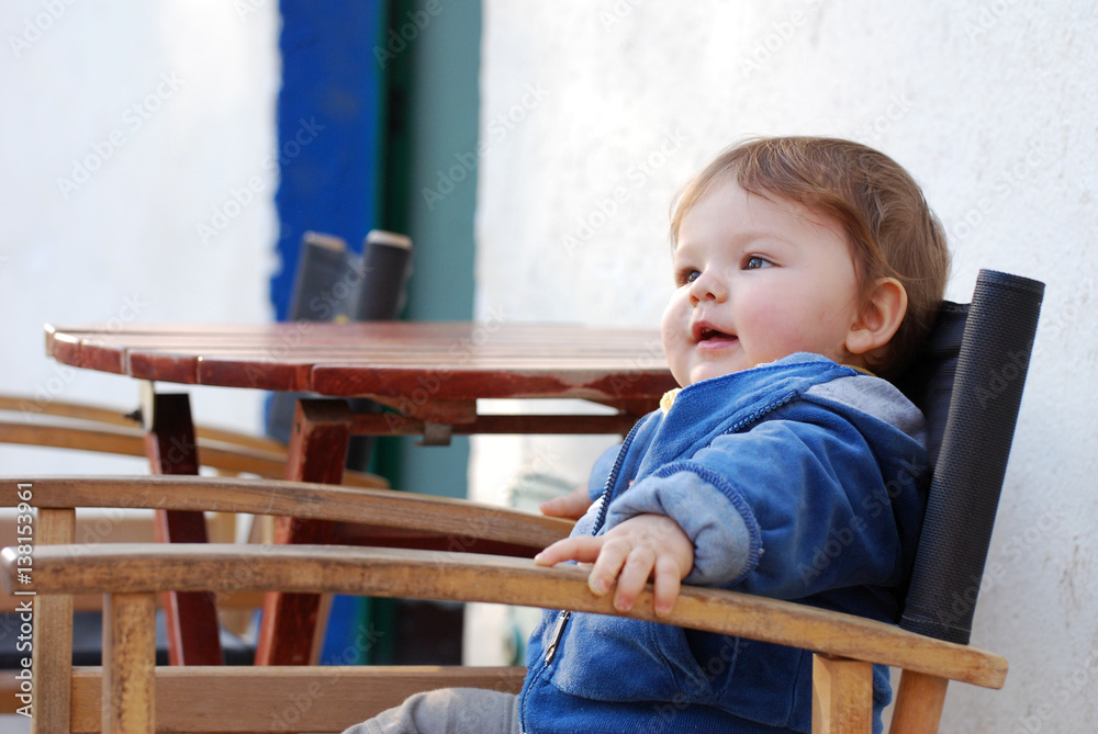 One Year boy sits in director chair in a public cafe in park One Year boy sits in director chair in a public cafe in park
