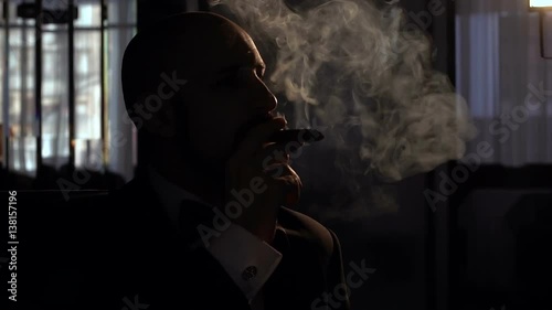 Adult man smokes a cigar in the dark with artificial light, slow motion. photo