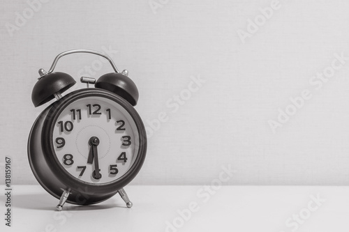 Closeup alarm clock for decorate show half past six or 6:30 a.m.on white wood desk and cream wallpaper textured background in black and white tone with copy space