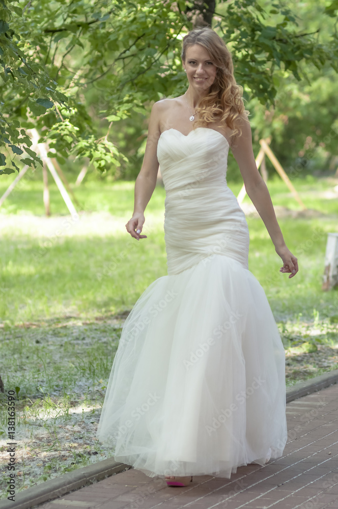 Young girl with red hair beautiful hair and makeup in a white dress of the bride in the park


