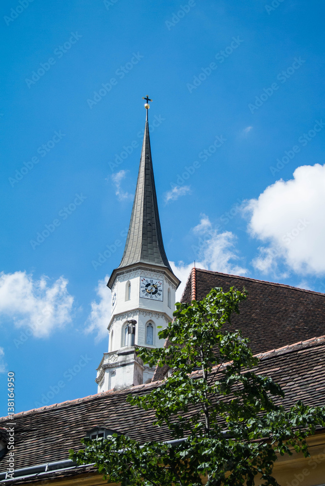 A church tower at the old center of Vienna above the tile roofs and a tree on a sunny summer day.