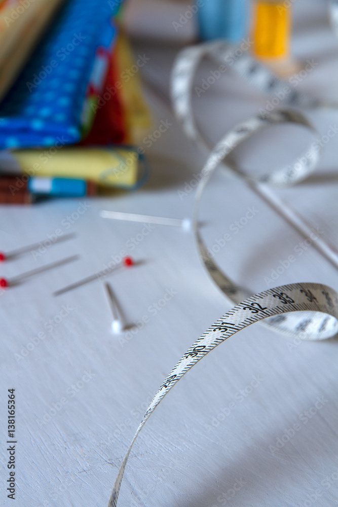 Colorful fabrics with pins, measuring tape and rolling cotton threads on white wooden table