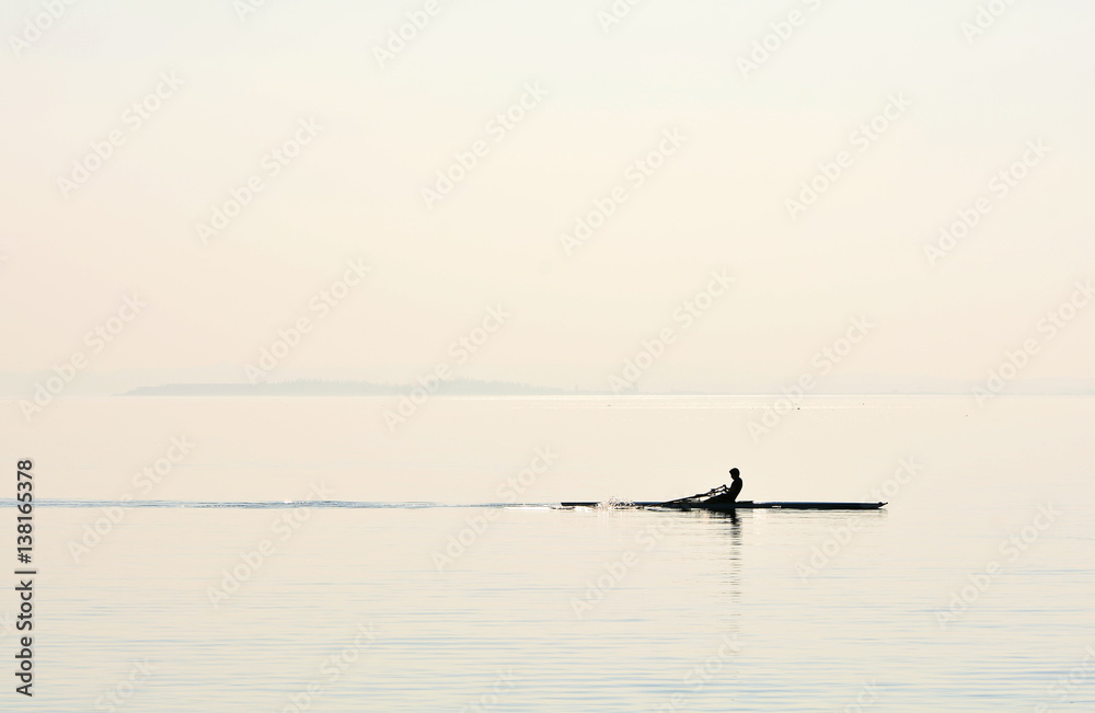 A man with his canoe paddling on the lake; backlit photo, silhouette.