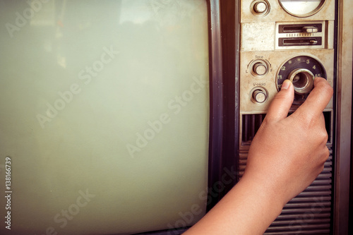 Woman hand fine tuning vintage television with control button. Retro image processed. photo