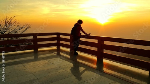 Silhouette of a short curly hair asian woman looking at dramatic sunrise landscape in the morning at view point balcony of Wat Pra That Doi Suthep, Chiang Mai, Thailand