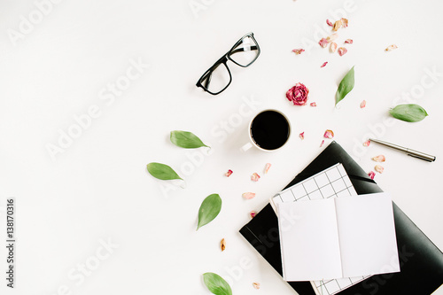 Blank notebook, red rose bud, glasses, leaves, coffee on white background. Entrepreneur home office table desk workspace. Flat lay, top view