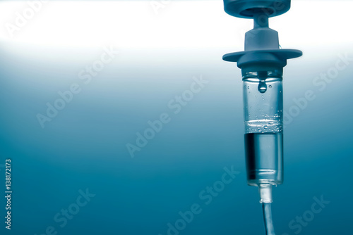 close up of a slow intravenous drip with a blurred lit neon in the background in a hospital room photo