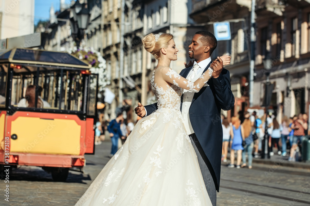 Naklejka premium Happy african American groom and cute bride dancing on street