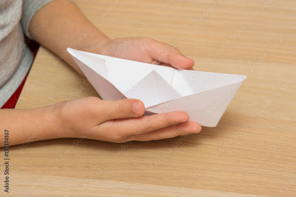 The child holds in his hands a paper boat, close-up The child holds in his hands a paper boat, close-up