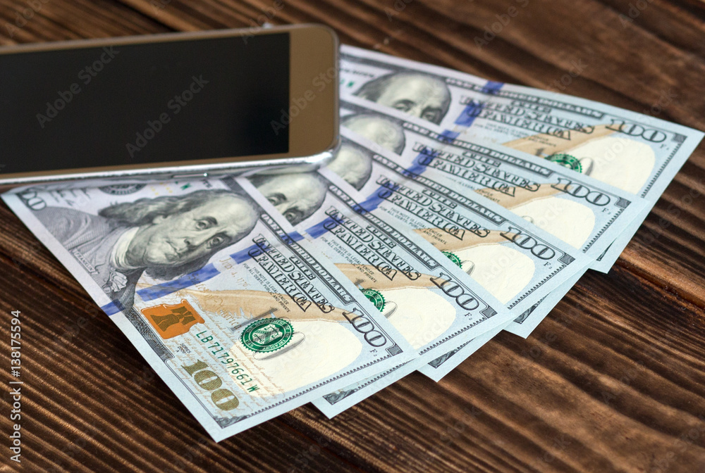 Smart phone with dollar banknotes on a brown wooden background Smart phone with dollar banknotes on a brown wooden background