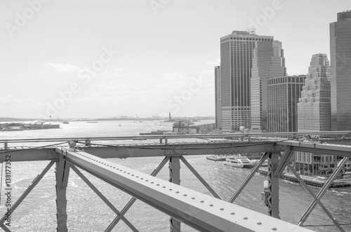 Manhattan skyline with the Statue of Liberty in the distance, seen from the Brooklyn Bridge in black and white