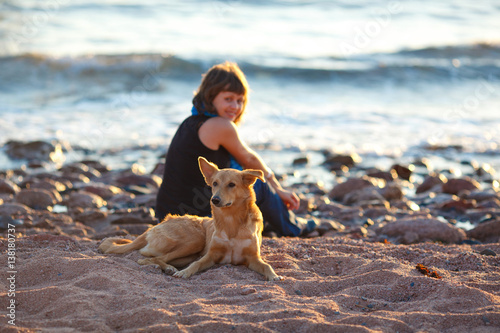 Stray dog sitting on the beach in front of a smiling young girl