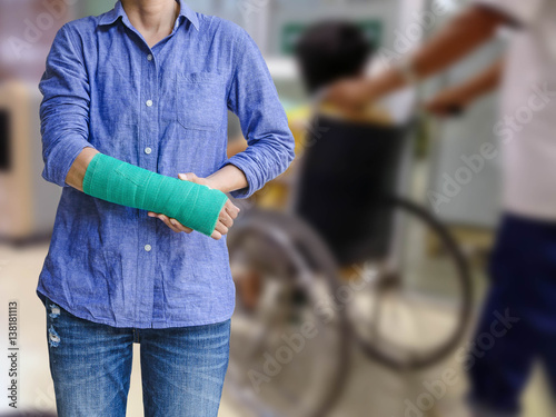 injured woman with green cast on hand and arm on abstract blur hospital room interior