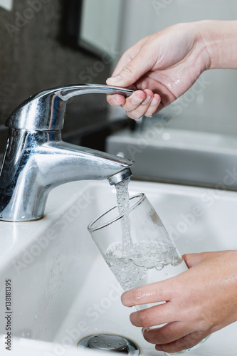 Woman filling a glass of water from a stainless steel or chrome tap