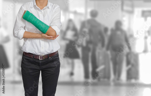 Injured woman with green cast on hand and arm on traveler in motion blur in airport interior background, ,body injury concept