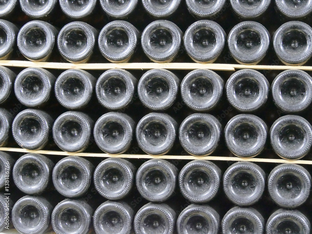 Old bottles of wine in rows in wine cellar. Rows of many wine bottles in winery cellar storage. Beautiful texture or background. Close up