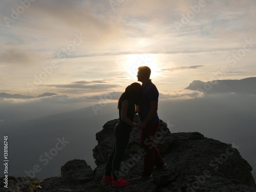 Silhouettes of young couple standing on a mountain and looking to each other on beautiful sunset background. Love of guy and girl. © olehslepchenko