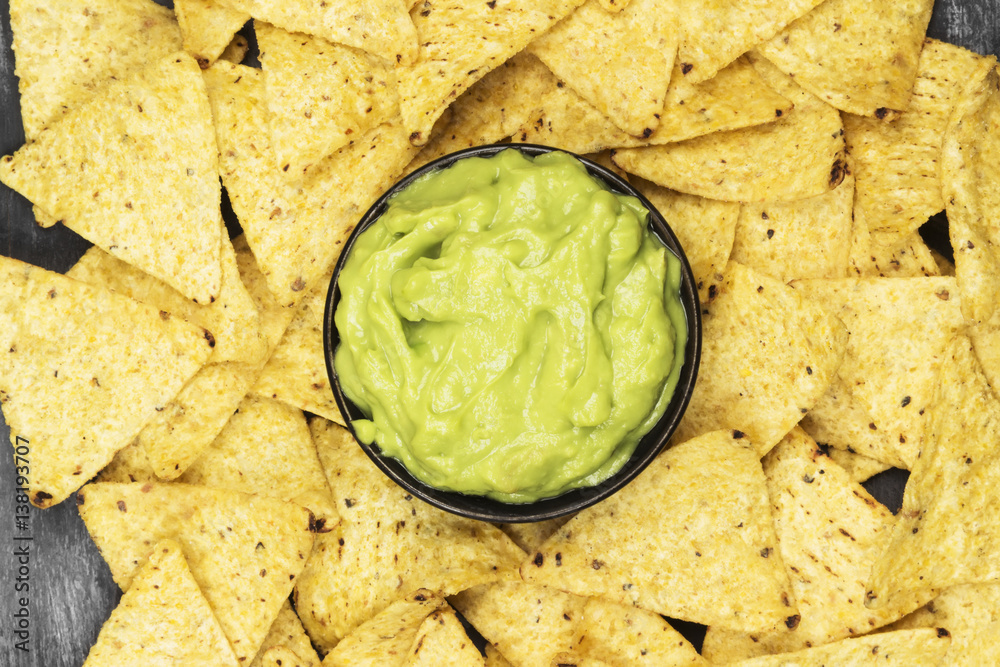 Traditional Latin American sauce guacamole in a bowl and nachos on a dark background. Top view, copy space. Food background Traditional Latin American sauce guacamole in a bowl and nachos on a dark background. Top view, copy space. Food background