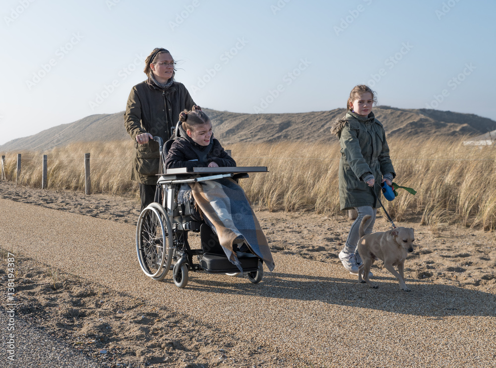 A disabled child in a wheelchair enjoying a walk along a beach path with her family A disabled child in a wheelchair enjoying a walk along a beach path with her family