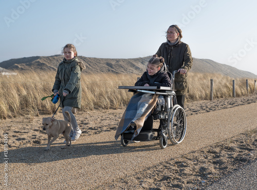 A disabled child in a wheelchair going for a coastal walk along the sand dunes with her family on a bright and sunny day